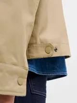 Campera utility de manga larga color beige, con cuello camisero de pana marrón. Tiene cierre de botones, dos bolsillos frontales con solapa y un interior forrado en poliéster reciclado. Cuenta con acabado repelente al agua.