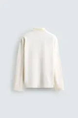 Polo de manga larga color rojo, confeccionado en tejido de algodón con estructura piqué, cuello solapa y cierre frontal de botonadura. Presenta aberturas laterales en el bajo.