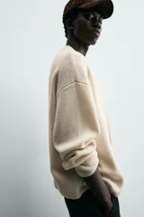 Cárdigan de punto color crema, con cuello pico, manga larga y cierre frontal de botones marrones. Presenta un calce relajado y acabados en rib.