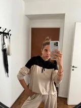 Sudadera con capucha de manga larga, color beige, con canesú negro en la parte superior de los hombros y capucha negra. Presenta cordones negros para ajustar la capucha.