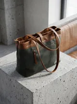 Cartera tipo tote de cuero vacuno, con diseño bicolor en gris y marrón. Cuenta con doble compartimento, cierre metálico, asas largas y una correa central decorativa con cierre de broche metálico. Incluye un detalle de etiqueta colgante de cuero.