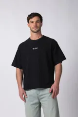 Remera de corte boxy y fit cuadrado, confeccionada en algodón grueso de alta calidad. Presenta un diseño minimalista en el frente con un pequeño logo circular y una estampa de gran tamaño en la espalda con la frase 'Designed in South America, Worldwide Clothes'.