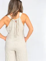 Mono largo de lino color beige, con escote en V, tirantes anchos, bolsillos laterales y silueta holgada. Cuenta con espalda ajustable mediante lazos.