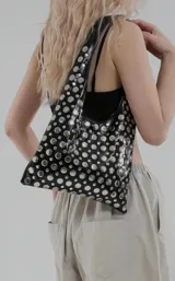 Cartera negra tipo tote bag con tachas circulares plateadas.