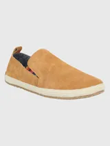 Alpargata Hush Puppies de gamuza color mostaza, con suela de yute trenzado y base de goma. Presenta un detalle elástico lateral con diseño multicolor y forro interior de algodón orgánico.
