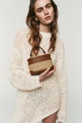 Bolso tipo vanity combinado en rafia y efecto cuero marrón, con cuerpo de tejido trenzado, detalles de pespuntes, asa de mano superior y cierre de cremallera.