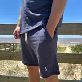 Short de tejido de punto con textura, color blanco, con bolsillos laterales y logo pequeño bordado en la pierna.