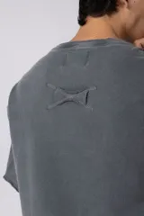 Remeron de corte oversized con cuello redondo y mangas cortas. Presenta un acabado de tela con efecto desgastado y costuras visibles en los bordes, con una etiqueta pequeña en el lateral inferior.