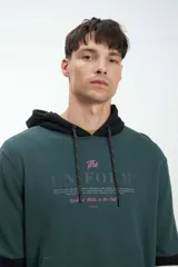 Canguro verde con capucha forrada en negro, cordones de ajuste trenzados y estampado frontal con la frase "The Uniform Youthful Thrills in the Chill 1956".