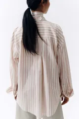 Camisa de corte oversize, con diseño de rayas verticales en tonos rosados, blancos y beiges, cuello clásico, mangas largas con puños abotonados y cierre frontal de botones.