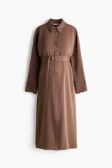 Vestido midi marrón de estilo camisero, con cuello, cierre frontal de botones, hombros caídos y mangas largas. Incluye un cinturón de tela con hebilla metálica de anillas en D.