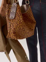 Cartera tipo hobo de cuero azul con textura granulada. Presenta un diseño holgado, con una correa de hombro bicolor que combina azul y rojo, sujeta por argollas metálicas. Incluye una placa metálica pequeña con el logo de la marca en la parte inferior frontal.