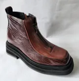 Botas cortas marca Lanka, confeccionadas en cuero vacuno color chocolate. Presentan una combinación de texturas, con paneles laterales de cuero grabado tipo reptil y frente liso. Cuentan con cierre frontal, puntera cuadrada y suela de plataforma dentada en color negro.