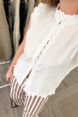 Blusa blanca sin mangas con cuello mao y volados en hombros y ruedo. Cierre frontal con botones.