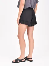 Short negro de tela liviana con cintura elástica fruncida y cordón ajustable con borlas. El ruedo tiene un volante con terminación de volado.