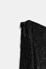 Falda midi negra de tiro medio, confeccionada en tejido de encaje con forro interior a tono. Presenta un bajo asimétrico con terminación en línea evasé y cierre lateral oculto.