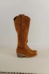 Bota estilo tejana de caña alta, confeccionada en gamuza, con taco cuadrado y diseño de costuras decorativas.