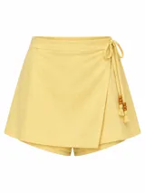 Short pollera color amarillo claro, con diseño cruzado tipo falda en el frente, cintura alta y cordones de ajuste laterales decorados con cuentas de madera y borlas.