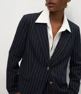 Blazer de sastrería estructurado color azul marino con estampado de rayas verticales blancas (risca de tiza). Presenta solapa clásica, cierre frontal con dos botones, bolsillos laterales con solapa y forro interno.