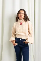 Polera de punto color manteca, con cuello alto, diseño de trenzas y flores en el frente, y mangas globo amplias.