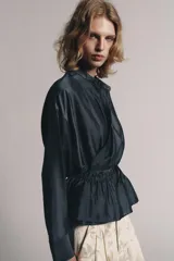 Blusa fluida cruzada de diseño envolvente, color gris oscuro satinado, con mangas largas y puños anchos. Cuenta con cuello mao y cordón ajustable en la cintura con lazada lateral.