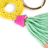 Llavero con argolla y mosquetón metálicos dorados, compuesto por un aro central de mostacillas amarillas y un colgante de borla con mostacillas en colores fucsia, verde agua y coral.