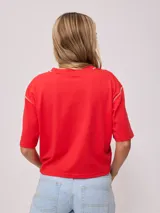 Remera blanca de algodón con corte cropped y calce holgado. Tiene cuello redondo con ribete azul y logo de la marca estampado en el pecho.