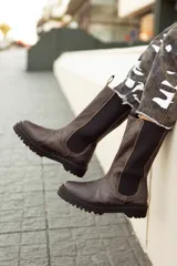 Bota de cuero color chocolate, de caña alta con elásticos laterales y tiradores en la parte superior. Suela de neolite color negro. Diseño artesanal fabricado en Uruguay.