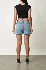 Short pollera de jean de tiro medio, color azul claro, con doble botón en la cintura y diseño de falda corta al frente con pantalón corto interno.