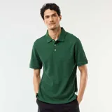 Remera polo de piqué de algodón color verde oscuro, de manga corta, con cuello camisero y cartera de tres botones. Presenta una textura sutil de líneas horizontales en relieve y una pequeña etiqueta decorativa en el borde inferior.