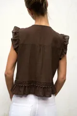 Blusa de cuello redondo y manga sisa con volantes, color marrón, con detalles de entredoses a tono, jaretas delanteras y cierre frontal con botones.