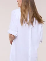 Vestido corto blanco de algodón, marca Dash, con cuello camisero, escote en V y bolsillos laterales. Presenta mangas tres cuartos y calce holgado con ruedo irregular.