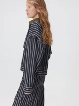 Campera de denim a rayas verticales con cuello de pana en color bordó. Presenta cierre frontal, mangas desmontables con cierre en los hombros, canesú en el pecho y bolsillos de parche cuadrados.