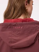 Campera rompevientos color bordó con cierre frontal, capucha con cordones ajustables y franjas laterales en tono más oscuro. Presenta puños elásticos y bolsillos frontales.