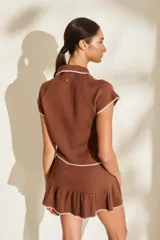 Falda corta de tejido de punto color marrón, con detalles de costuras a contratono en blanco y diseño con volados fruncidos en el ruedo.