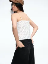 Top lencero de tirantes finos con estampado floral pequeño sobre fondo blanco. Presenta detalles de volados en el pecho y una textura acanalada sutil.