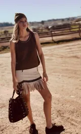 Bolso tipo bucket de cuero color marrón con tachas plateadas. Tiene correa larga regulable para usar al hombro y cierre con cordón ajustable.