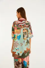 Camisa de viscosa con estampado ilustrado de escenas de Río de Janeiro, que incluye playa, morros y elementos tropicales. Cuenta con cuello camisero, botones frontales y mangas cortas holgadas.