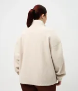 Campera deportiva de sherpa color beige, con cuello alto, cierre frontal completo y bolsillo con cierre en el pecho. Presenta un corte boxy holgado, mangas largas y acabado de textura suave.