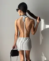 Vestido corto de tela brillante plateada con cuello drapeado, diseño halter y espalda descubierta.