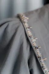 Chaqueta gris de silueta femenina con mangas abullonadas, cuello redondo y cierre frontal con botones forrados. Presenta detalles de bordado artesanal a mano en los hombros y solapas.