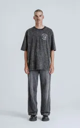 Remera negra con efecto nevado, de manga corta y cuello redondo, con calce oversize. Presenta un estampado trasero inspirado en la carta del Tarot "El Mundo" (XXI), con una figura femenina, un globo terráqueo y la frase "El Mundo".