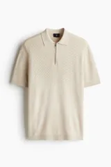 Remera polo de manga corta confeccionada en punto fino de mezcla de algodón, con cuello acanalado y cierre frontal parcial con cremallera. Presenta una textura sutil en relieve y terminaciones acanaladas en mangas y bajo.