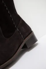 Bota alta de cuero color chocolate, con diseño de caña recta y detalle de pespuntes decorativos a lo largo de la pierna. Cuenta con un taco bajo cuadrado y cierre lateral.