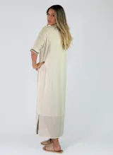 Vestido midi de punto color beige, con cuello solapa, mangas cortas y cierre frontal con botones. Presenta detalles de costuras y terminaciones en color mostaza, además de un diseño calado en el sector inferior de la falda.