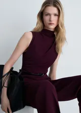 Mono largo color borgoña, con cuello Perkins drapeado, sin mangas, corte recto, cinturón con hebilla y cierre de cremallera en la parte posterior.