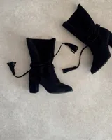 Botín de gamuza negro con taco cuadrado, caña media y tiras finas con borlas para atar alrededor del tobillo.