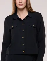 Camperita liviana de corte recto y acabado crepé color blanco, con cuello camisero clásico y cierre frontal de botones metálicos dorados. Presenta bolsillos en el pecho con solapa y mangas largas con puños abotonados.