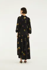 Vestido largo negro de mangas largas con puños elastizados, escote en V con lazo regulable y falda amplia con recorte fruncido, confeccionado en tejido liviano con estampado floral e inspirado en la selva.