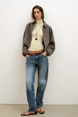Chaqueta de corte corto y diseño abullonado en color marrón oscuro, con cuello solapa, mangas largas con puños elásticos y cierre frontal con cremallera metálica. Cuenta con bolsillos delanteros de doble vivo.